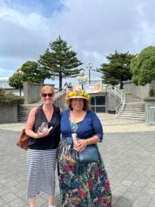 Two women smiling outdoors, one wearing a fruit hat