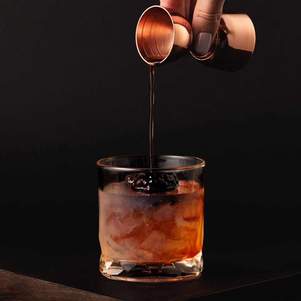 Pouring cocktail over ice with blackberry