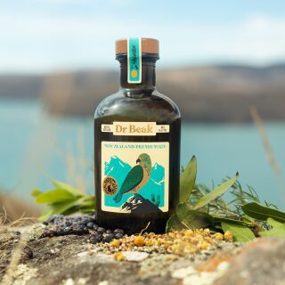 A bottle of Dr Beak Gin sitting on a rock with water in the background.
