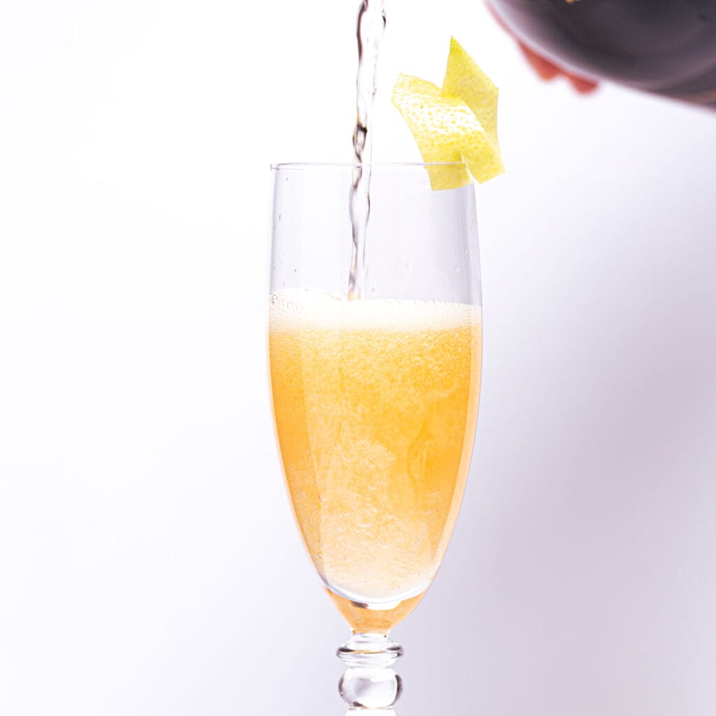 Pouring mimosa cocktail with lemon twist garnish