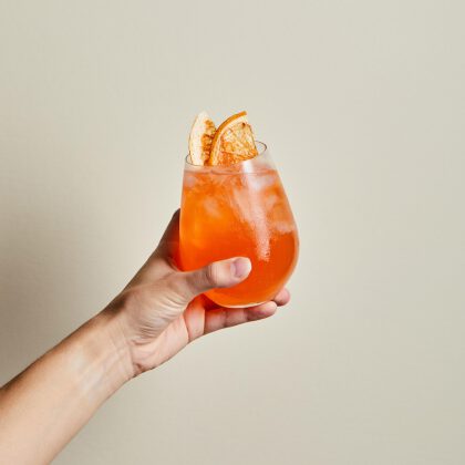 Hand holding orange cocktail with citrus garnish.