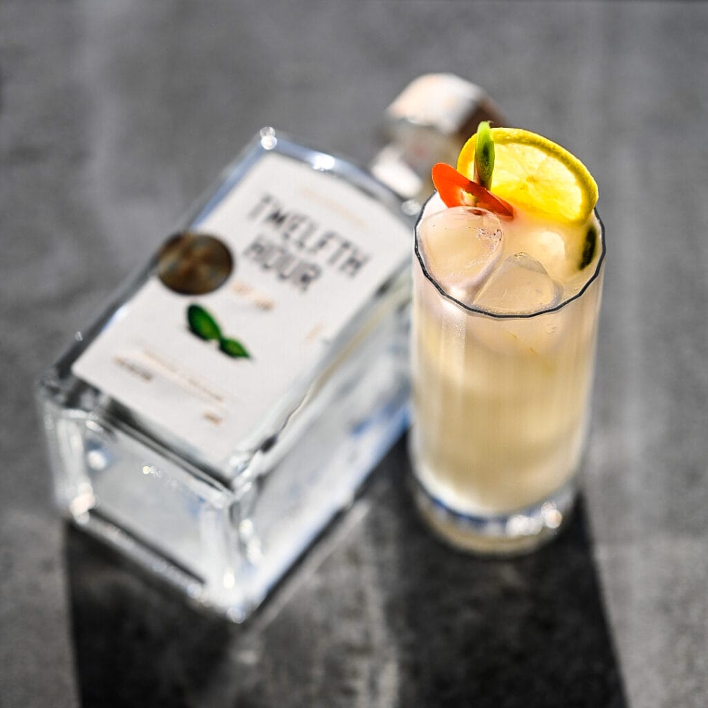 Cocktail with lemon, pepper garnish beside liquor bottle.