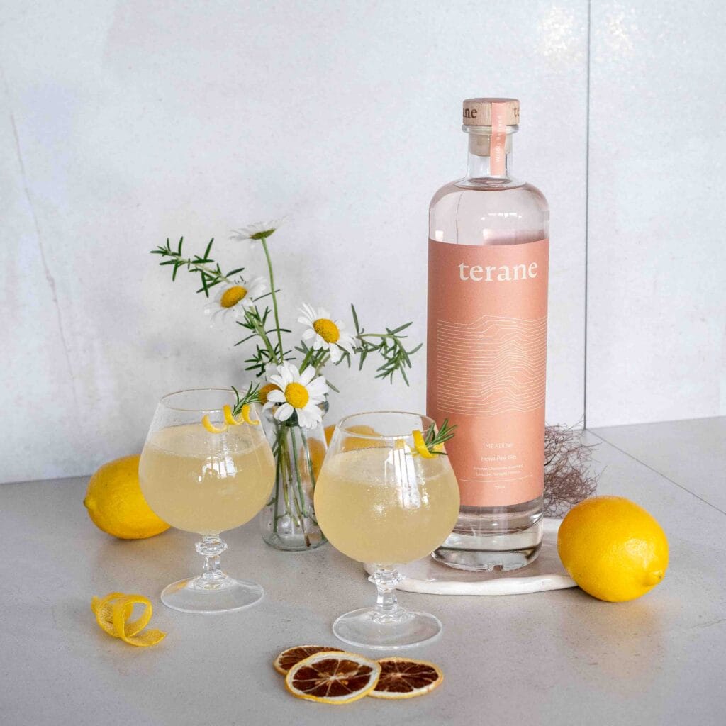 A bottle of Terane Gin with flowers and 2 cocktails.